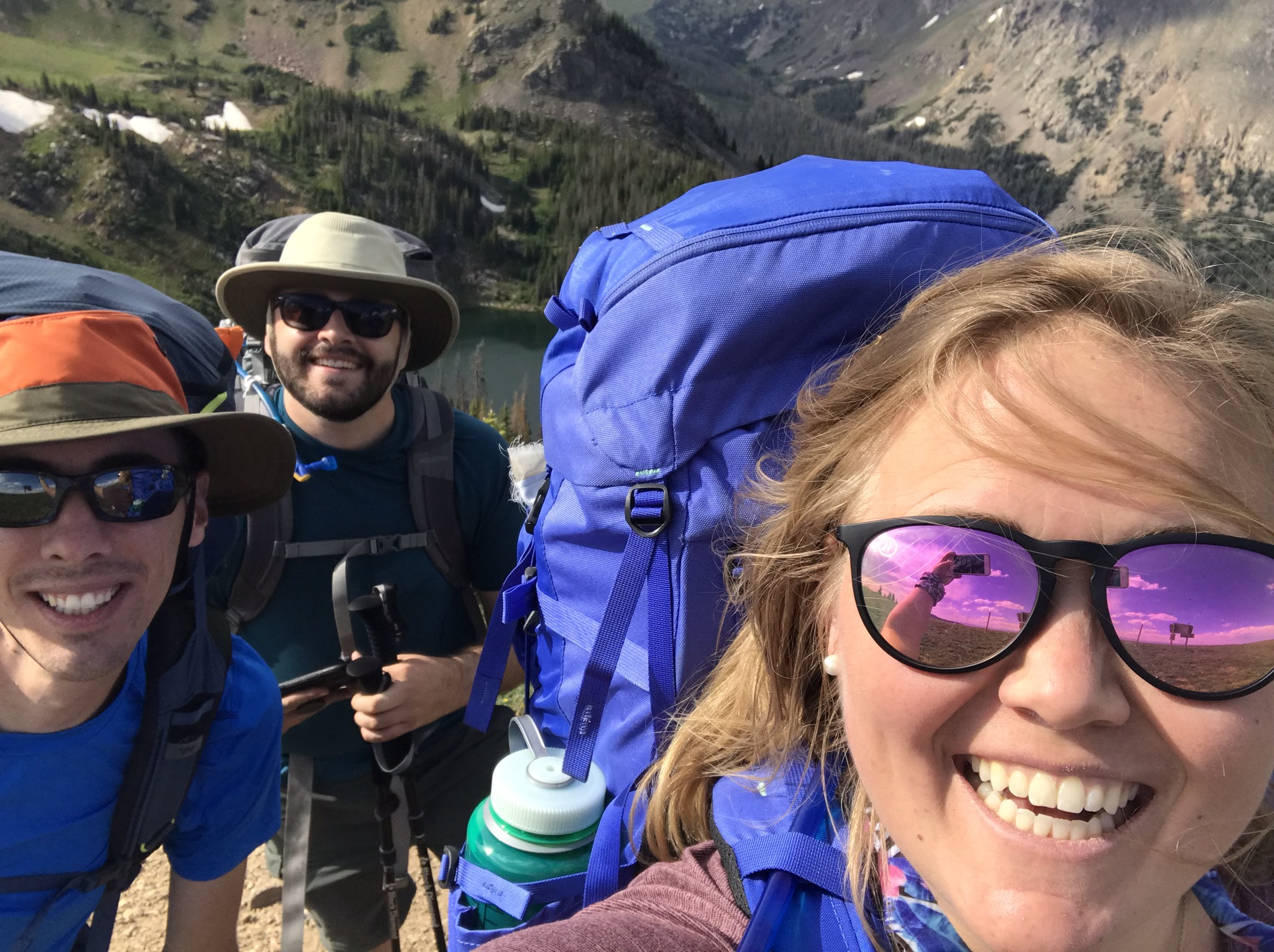 A selfie including three smiling friends, all wearing sunglasses and wearing large backpacks.